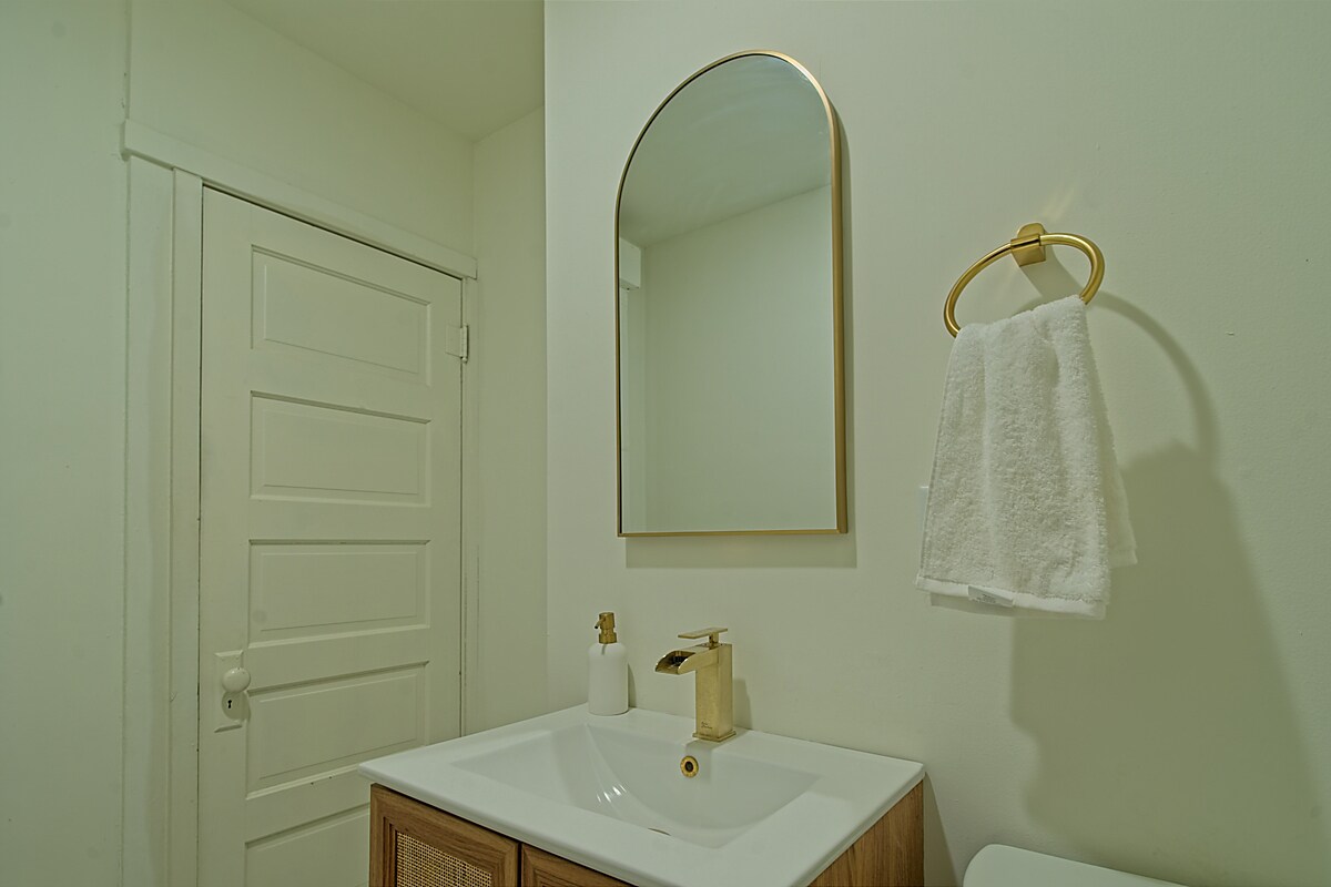 Refreshed restroom with vanity, arched mirror, and brass fixtures