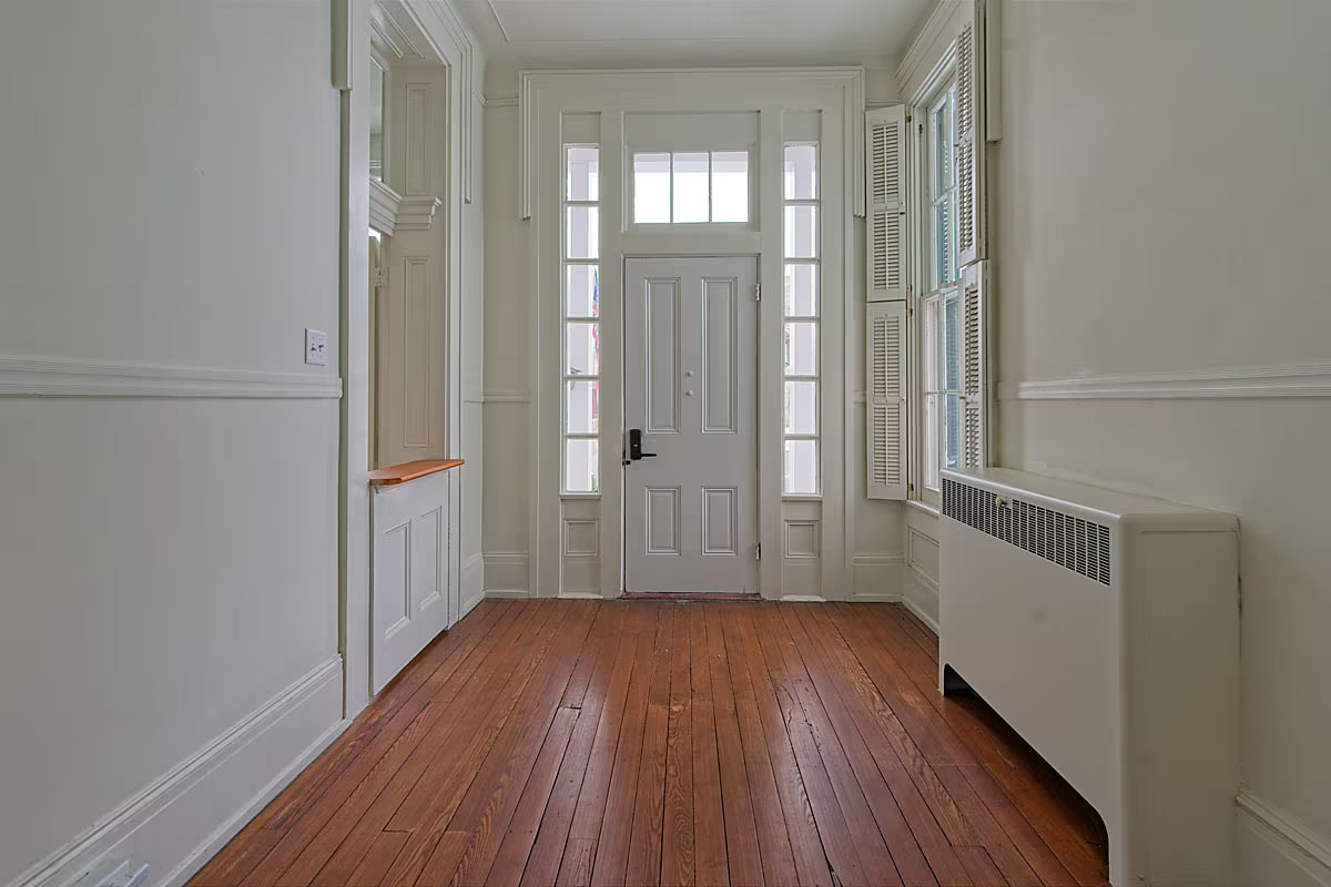 Entry foyer with paneled front door, restored hardwood floors, and original radiator