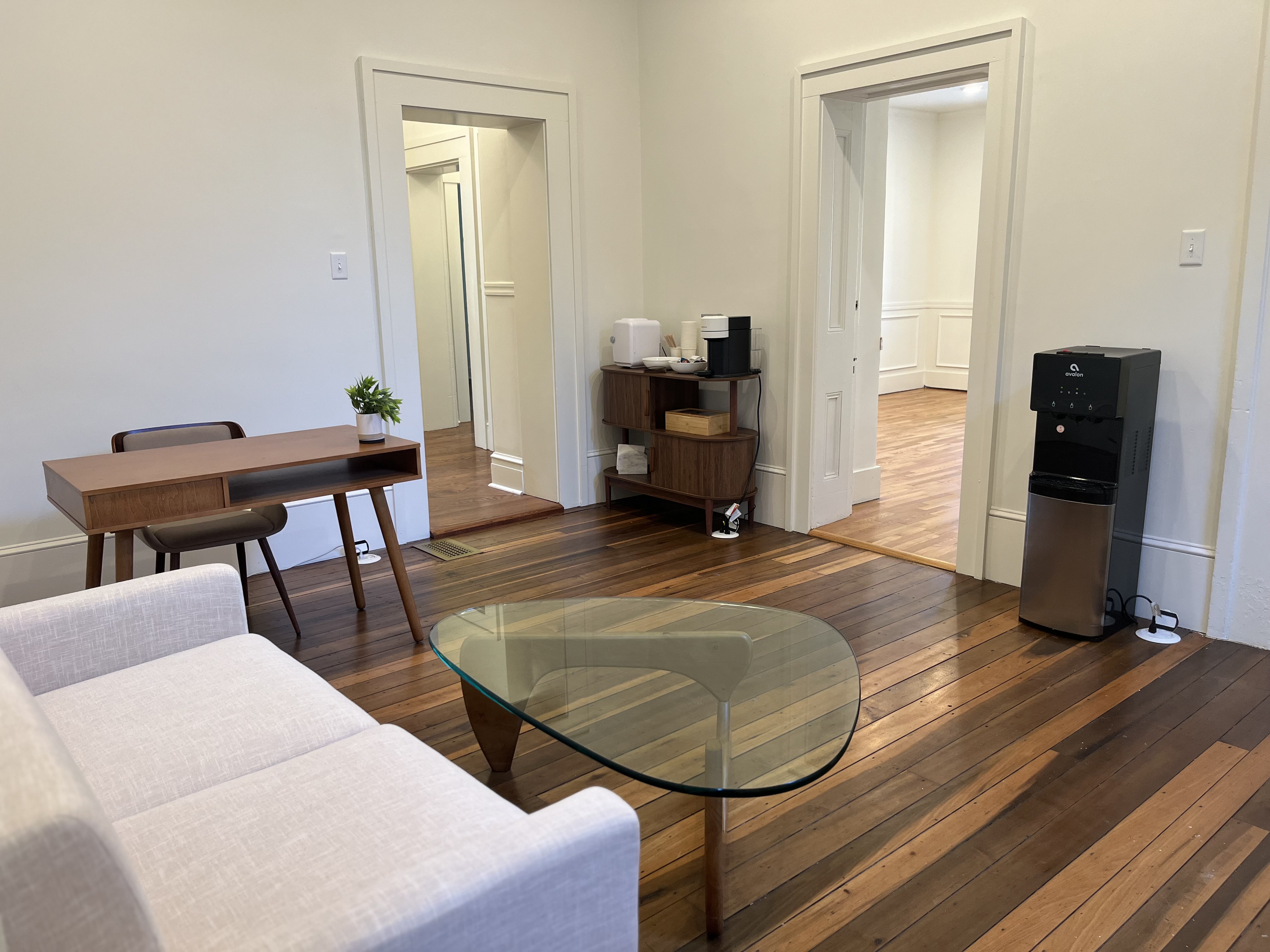 Common area with restored hardwood floors, coffee bar, sofa seating, and glass coffee table